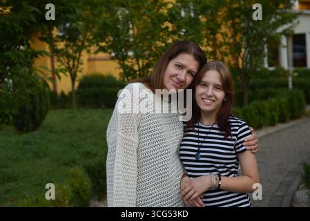 Una madre e una figlia condividono un momento di gioia insieme in un giardino. Lo sfondo è caratterizzato da una vegetazione vivace, che migliora la calda e intima scena familiare Foto Stock