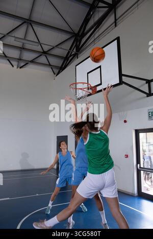 Diverse atlete che saltano verso il cerchio mentre le difensori alzano le braccia sul campo da basket Foto Stock