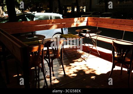 Terrazza caffetteria all'aperto con tavoli in legno, sedie e cuscini alla luce del sole sotto gli alberi. Belgrado, Serbia. Foto Stock