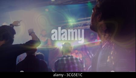Cinque concertatori maschili di fronte al palco che puntano in un locale di musica dal vivo, con capriate luminose e luci a raffica Foto Stock