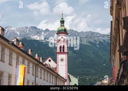 Una storica torre dell'orologio barocco a Innsbruck, Austria, che sorge sopra gli edifici della città vecchia con le Alpi Nordkette sullo sfondo. Foto Stock