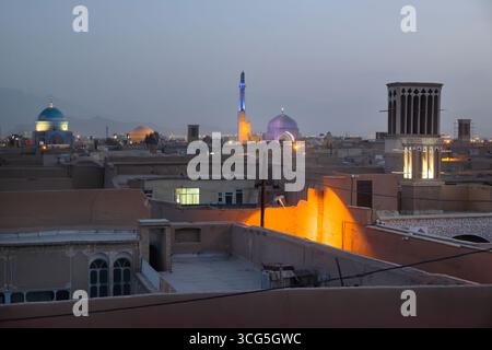 L'incantevole skyline di Yazd, Iran, mostra moschee illuminate e windcatcher al tramonto Foto Stock
