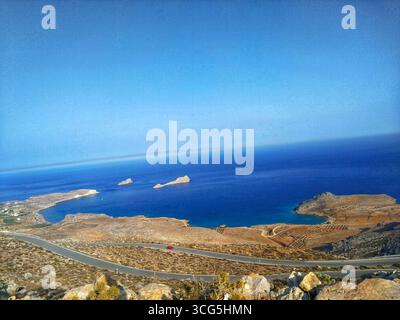 Vista panoramica di una tortuosa strada costiera, terreno roccioso e del Mar Mediterraneo con piccole isole a Creta orientale, Grecia. Foto Stock