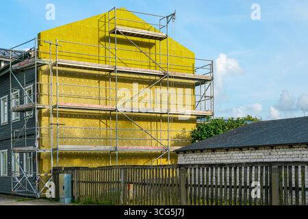 Parete esterna rivestita con isolamento termico giallo e ponteggi, evidenziando i lavori di ristrutturazione a basso consumo energetico di un edificio residenziale Foto Stock
