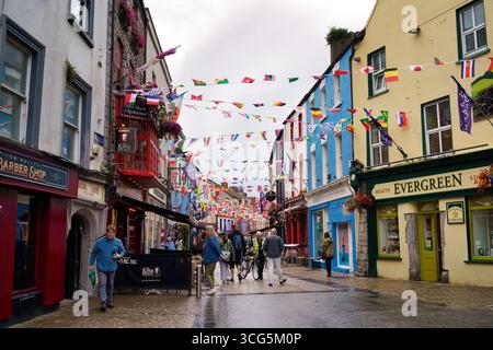 Una vivace scena di strada a Galway, in Irlanda, piena di edifici colorati e bandiere. Foto Stock