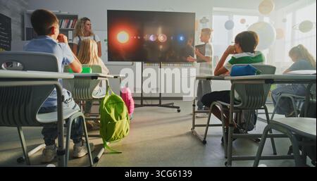 Primary School Boy con tablet computer che mostra la conoscenza dell'astronomia in prima classe e insegnante con schermo digitale. Bambini che ascoltano la presentazione, imparare a conoscere il sistema solare, i pianeti. Foto Stock