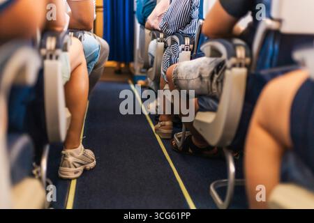 I viaggiatori sono seduti su un aereo, con le gambe visibili dalla corsia. L'atmosfera indica un'anticipazione durante la preparazione dell'aeromobile Foto Stock
