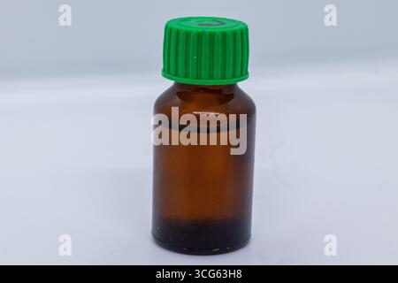 Flacone in vetro ambrato con tappo verde, ideale per la conservazione di oli essenziali, medicinali o liquidi. Isolato su sfondo bianco. Foto Stock