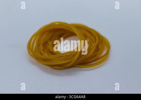 Primo piano di elastici gialli luminosi avvolti insieme su uno sfondo bianco pulito. Forniture elastiche per ufficio perfette per l'organizzazione, il raggruppamento e le statistiche Foto Stock