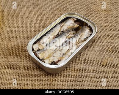 Una lattina aperta di sardine posta su tessuto di bavone; le sardine sono allineate in modo ordinato, evidenziando la consistenza argentata, l'olio e il contenitore metallico. Foto Stock