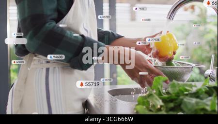 Donna che indossa una camicia a quadri risciacquando il peperone al lavello della cucina, con bolle di notifica digitali Foto Stock