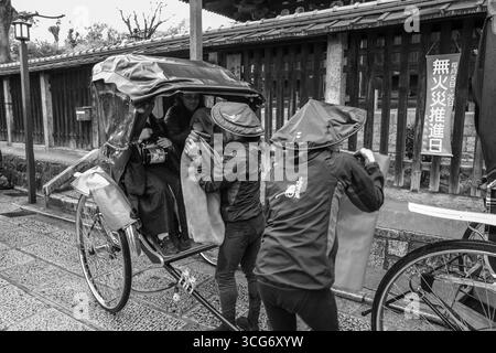 Fotografia in bianco e nero di persone locali in un risciò tradizionale giapponese su una strada piovosa, Yasaka Kamimachi, Higashiyama Ward, Kyoto, Kansai, ho Foto Stock