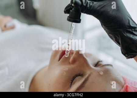 Un cosmetologo sta facendo cadere il siero da un contagocce sul viso di un paziente durante una procedura cosmetica Foto Stock