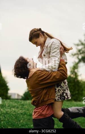 Una giovane coppia si diverte a vicenda mentre passeggiano mano nella mano attraverso un parco lussureggiante. Foto Stock