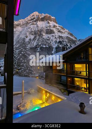 Balcone con vista sulla casa e piscina all'aperto illuminata e il monte Wetterhorn in una giornata invernale di neve a Dusk a Grindelwald, Canton Berna, Foto Stock