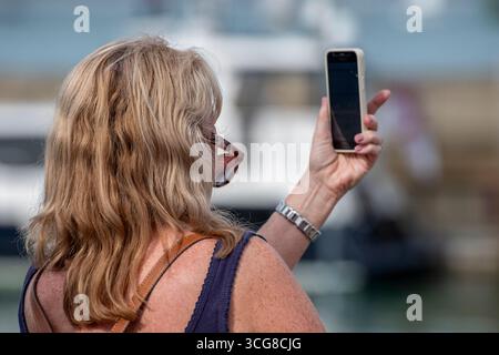 donna di mezza età che utilizza uno smartphone per scattare una foto da selfie, bionda che usa lo smartphone per scattare una foto Foto Stock