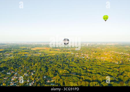 Sint-Martens-Latem, Belgio - 25 agosto 2025: Veduta aerea di due mongolfiere che volano sopra una vivace tettoia verde, la scena è immersa nella morbida Foto Stock