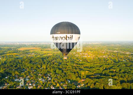 Sint-Martens-Latem, Belgio - 25 agosto 2025: Veduta aerea di una mongolfiera a marchio dumobil che si sposta serenamente su un arazzo verdeggiante di fitta foresta e tetti sparsi. Foto Stock