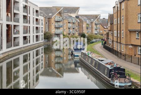 Londra, Regno Unito - 23 agosto 2025 - una scena tranquilla lungo il Grand Union Canal, con edifici residenziali che costeggiano la riva del canale con le barche a vela moore Foto Stock