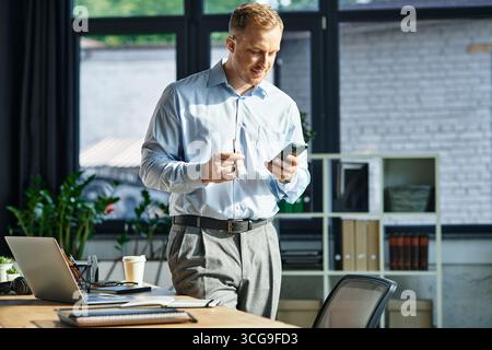Un giovane affascinante controlla meticolosamente il suo telefono mentre gestisce le attività in un ufficio affollato. Foto Stock