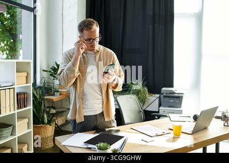 Un bel giovane in un elegante ufficio controlla il telefono, con grande attenzione e attenzione. Foto Stock