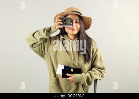 Felice viaggiatrice asiatica con bagagli, macchina fotografica, passaporto, biglietto d'imbarco e telefono cellulare isolato su sfondo grigio. Hap femminile indonesiana Foto Stock