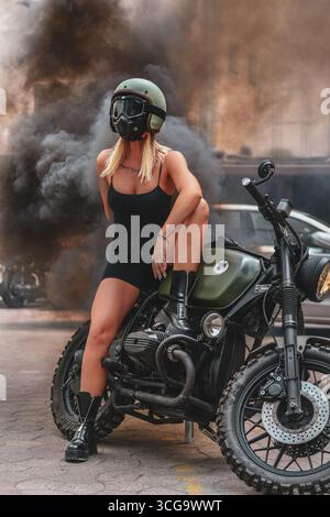 Donna seduta su una motocicletta BMW personalizzata con casco e maschera, fumo sullo sfondo, Serbia Foto Stock