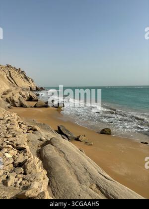Spiaggia di sabbia dorata con onde turchesi e scogliere di arenaria lungo la costa del Golfo Persico nel sud dell'Iran. Foto Stock