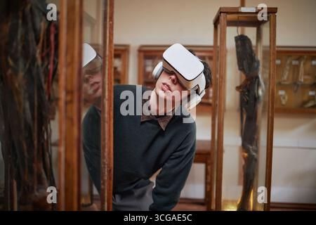 Young Caucasian Man Exploring Museum Exhibit Using Virtual Reality Headset Foto Stock