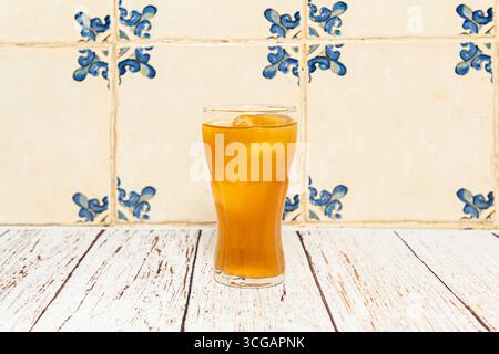 limonata in una caraffa di vetro con cucchiaio di legno, circondata da limoni interi ed erbe fresche in luce naturale diffusa Foto Stock