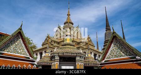Una splendida vista di un tradizionale tempio tailandese con un'architettura intricata, caratterizzato da piastrelle colorate e guglie ornate contro un cielo blu Foto Stock