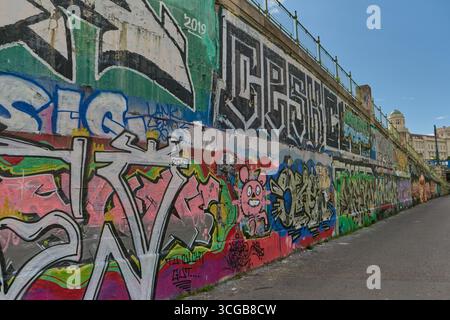 Colorate opere d'arte di graffiti coprono le pareti del fiume a Vienna, con un cielo azzurro e una vivace atmosfera urbana. Foto Stock