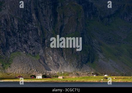 Le piccole case colorate sono in netto contrasto con le torreggianti scogliere e le pendici di un fiordo norvegese. Flakstad lofoten norvegia Foto Stock