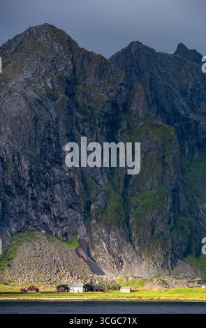 Le piccole case colorate sono in netto contrasto con le torreggianti scogliere e le pendici di un fiordo norvegese. Flakstad lofoten norvegia Foto Stock