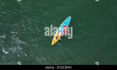Evento di stand up paddleboard con concorrenti, tavole e spettatori sulla spiaggia di Dorset, Inghilterra, vista dall'alto Foto Stock
