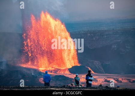 I visitatori si riuniscono in un punto panoramico per ammirare le fontane di lava calda che si estendono a 1000 metri dal cratere Halemaumau prima dell'alba, il vulcano Kilauea, Hawaii, Stati Uniti Foto Stock