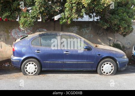 Macchina sporca e abbandonata su una strada pubblica. Veicolo sporco e abbandonato con pneumatici sgonfi, parcheggiato davanti a un muro. Scena urbana. Foto Stock