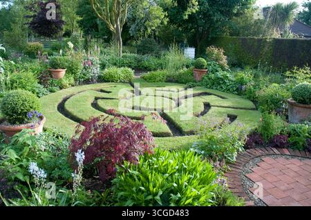 Un labirinto splendidamente curato caratterizzato da siepi verdi e piante colorate è esposto in un giardino sereno, che fornisce un'atmosfera rilassante. Foto Stock