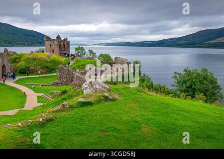 I turisti visitano le rovine del castello medievale di Urquhart arroccato sul lago Loch Ness nelle Highlands scozzesi in un giorno coperto. Foto Stock
