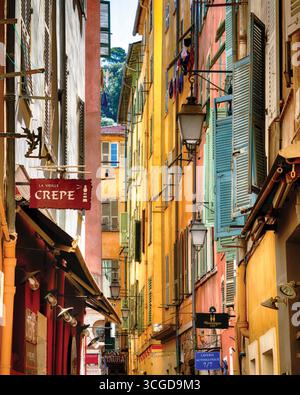 Strada stretta con lampade, tende in legno e case color pastello, centro storico di Nizza, Foto Stock