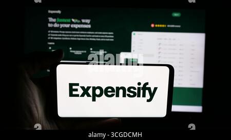 In questa immagine, una persona ha in mano un cellulare con il logo della società di gestione spese Expensify Inc. Sullo schermo davanti alla pagina Web. Foto Stock