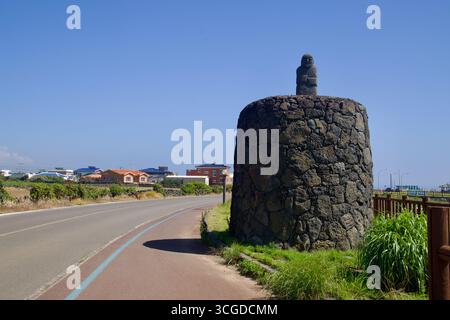 La frangiflutti del porto di Sindo si estende nelle acque blu della costa occidentale di Jeju, un faro rosso arroccato sopra tetrapodi di cemento, mentre le piscine di marea riempiono il jagg Foto Stock