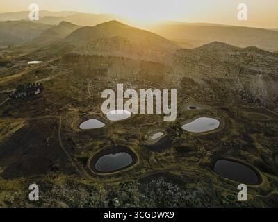 Vista aerea di numerosi stagni sparsi nel paesaggio aspro, con luce del sole dorata che baciano le montagne lontane, Aaqoura, il Governatorato del Monte Libano, Libano. Foto Stock