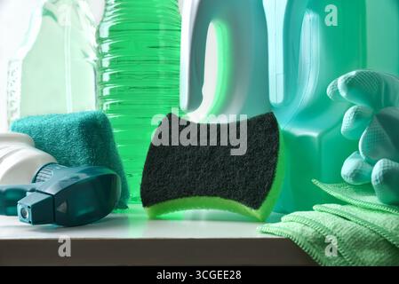 Dettaglio degli strumenti di pulizia come spugnette, guanti e panno e quattro bottiglie di plastica con prodotto disinfettante su un tavolo bianco. Vista frontale. Foto Stock