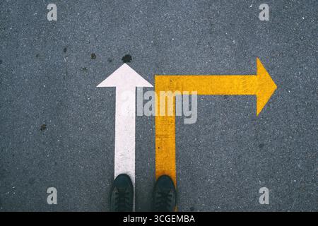 Frecce bianche e gialle sull'asfalto che mostrano direzioni diverse. Frecce dipinte sulla strada che simboleggiano la scelta e la direzione. Vista dall'alto. Foto Stock