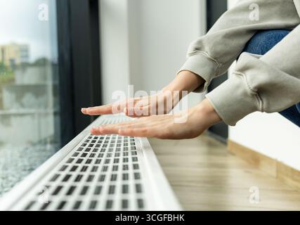 radiatore di riscaldamento nell'appartamento, la persona porta le mani in un maglione caldo al radiatore per controllare quanto caldo.costi di riscaldamento e utenze in inverno Foto Stock
