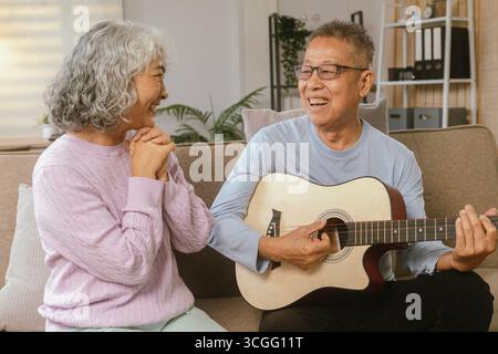 Felice coppia senior che si è ritirata insieme suonando strumenti musicali a casa a Bright Sunshine Foto Stock