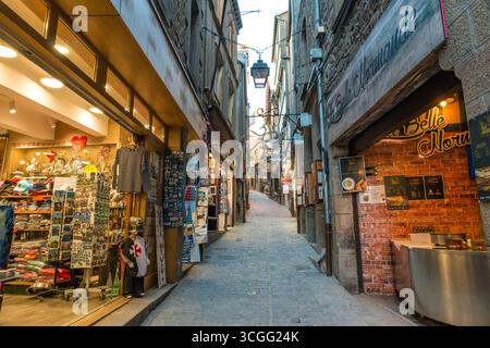 Una vista sulla stretta e tortuosa strada principale di Mont-Saint-Michel, la grande Rue, che conduce verso la sezione superiore. La strada di ciottoli vuota, fiancheggiata da... Foto Stock