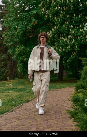 Un giovane con i capelli ricci passeggia in un parco vivace, godendo della bellezza della natura. Foto Stock