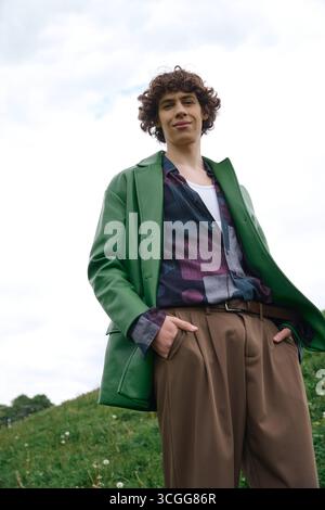 Un giovane con i capelli ricci si muove all'aperto, trasudando stile e sicurezza. Foto Stock